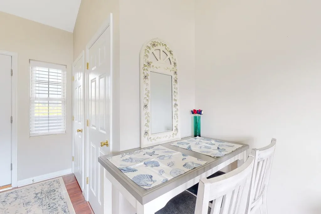 A bright dining area with a table, chairs, and a decorative wall mirror.