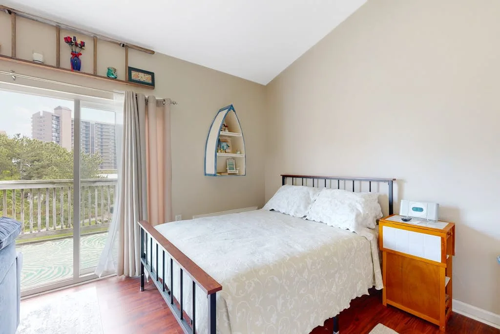 A bedroom with a bed beside a sliding glass door opening onto a balcony.