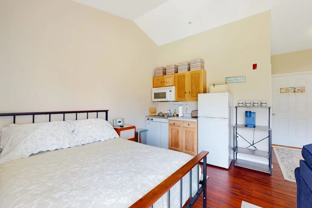 A bedroom with a bed, kitchenette, and refrigerator.