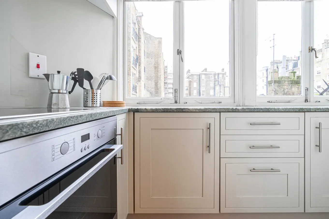 A bright kitchen with a built-in oven beneath the counter and large windows.