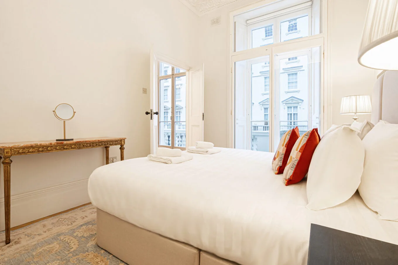 A bright bedroom features a neatly made bed beside tall windows.