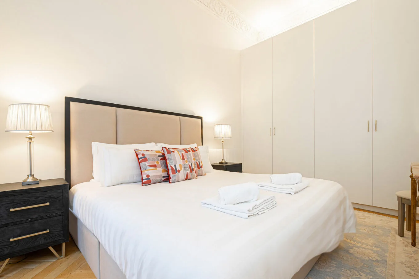 A bedroom with a large bed, bedside lamps, and built-in wardrobes.