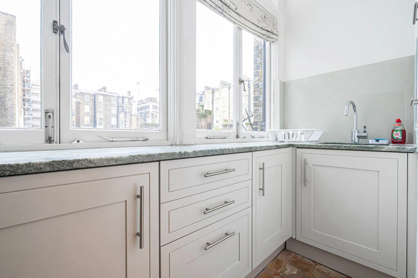 A bright kitchen with white cabinets, a countertop, and windows above the sink.