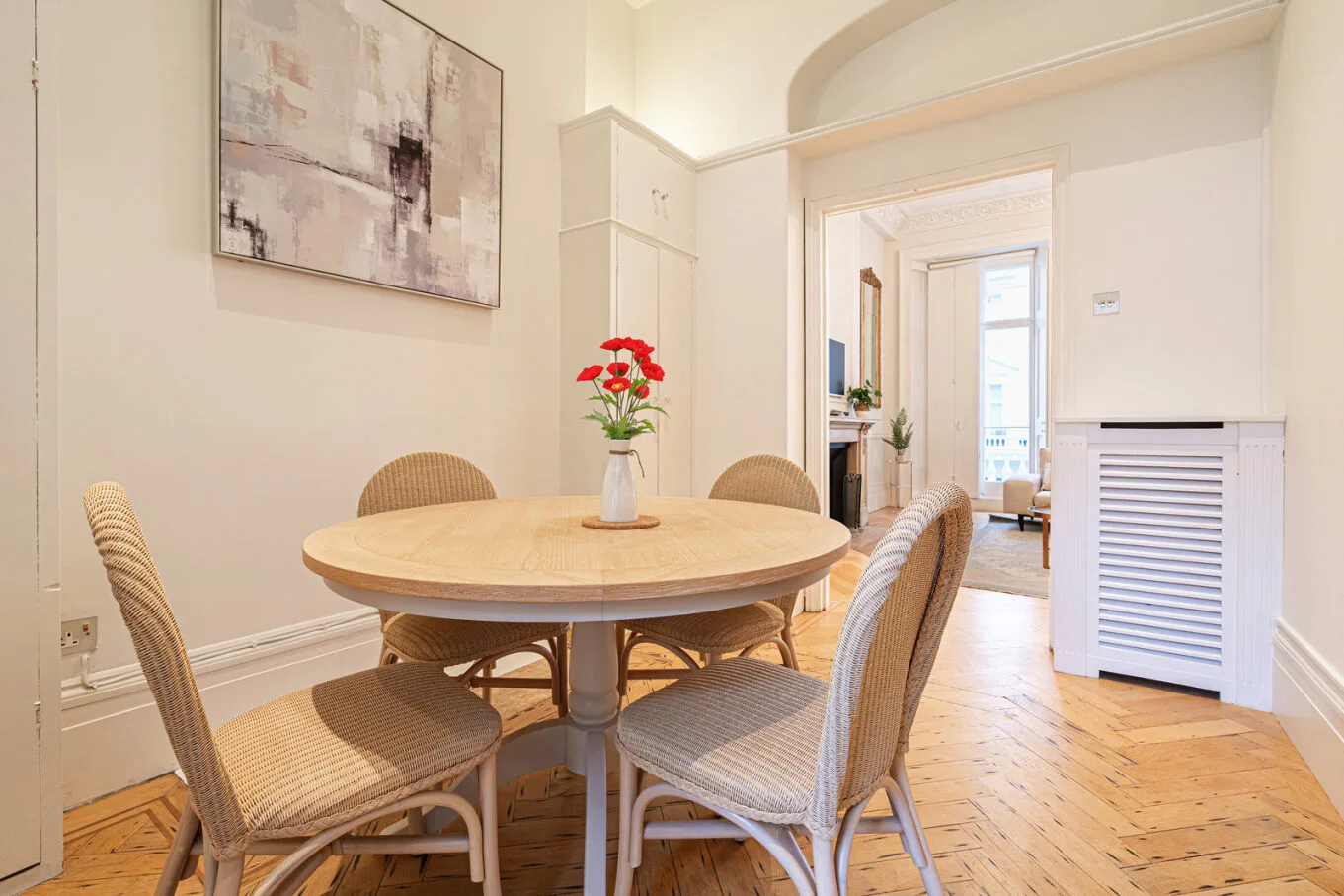 A bright dining area with a round table, woven seating, and flowers.