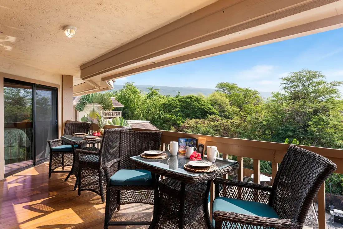 A covered outdoor dining area with a table and seating overlooks leafy trees.