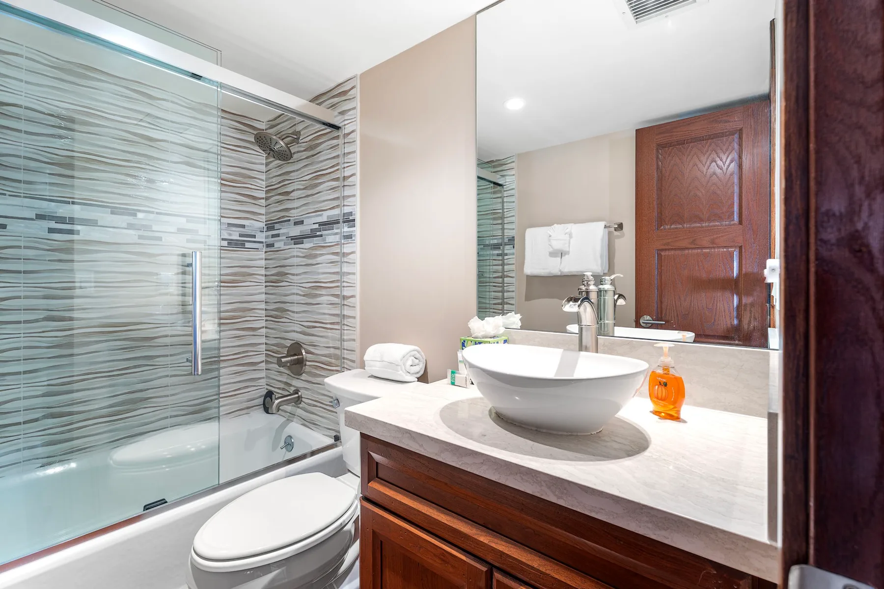 A bathroom with a glass shower, toilet, and vessel sink.