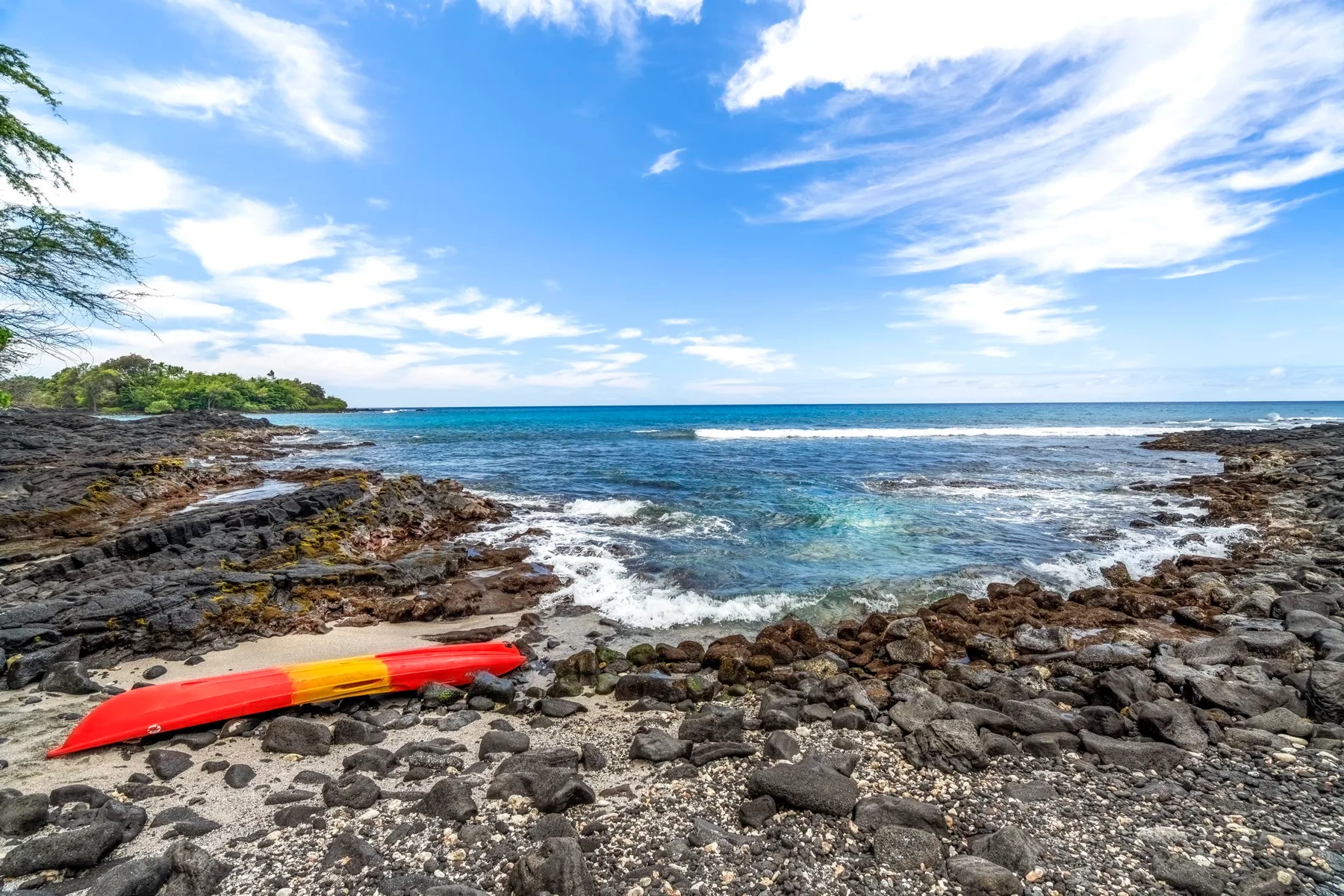 A rocky shoreline meets the ocean, with a colorful kayak resting on the shore.