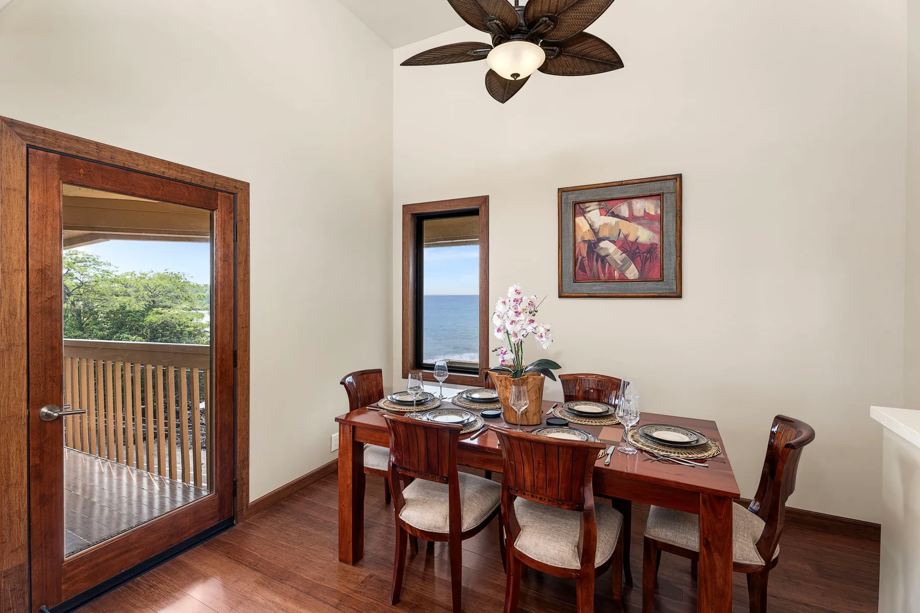 A dining area with a wooden table set beside windows overlooking greenery and the ocean.