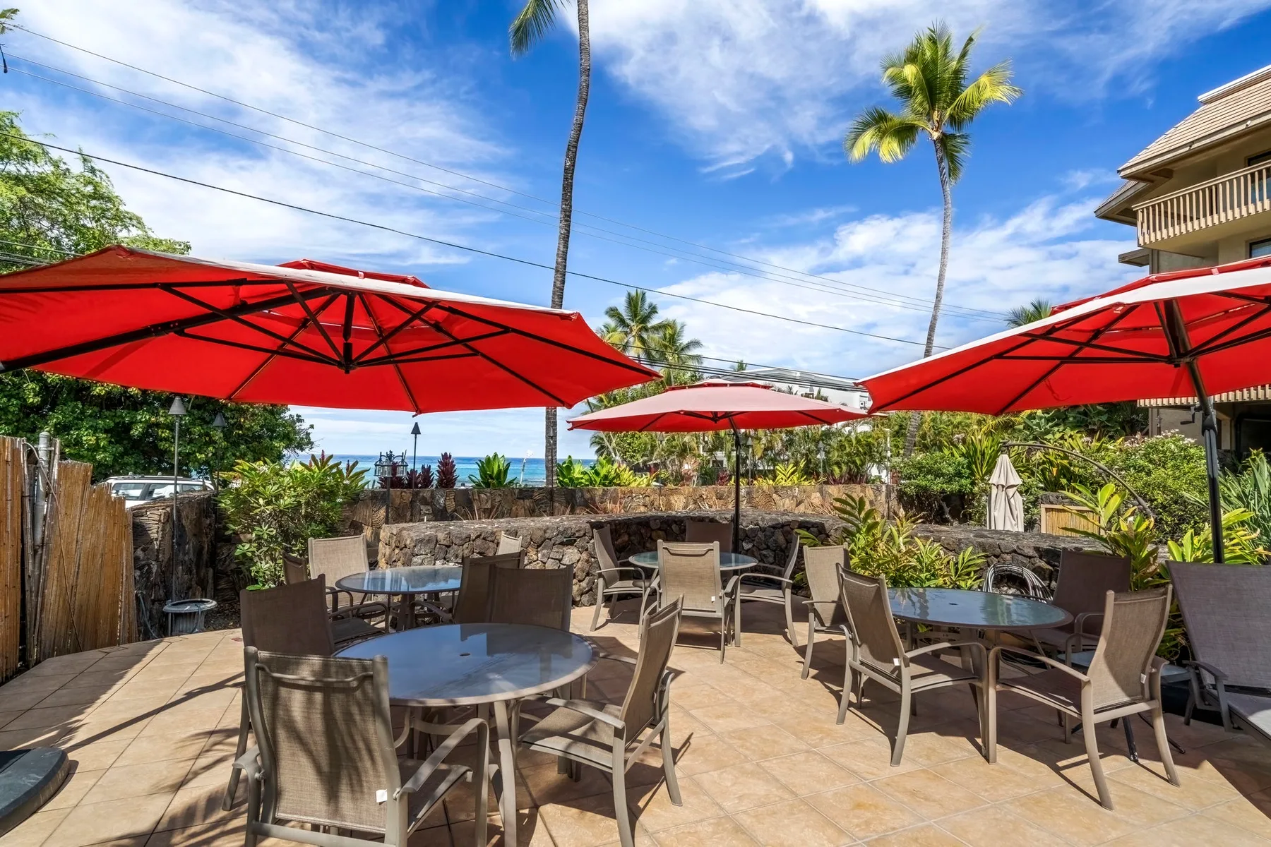An outdoor patio has tables and seating beneath large red umbrellas.