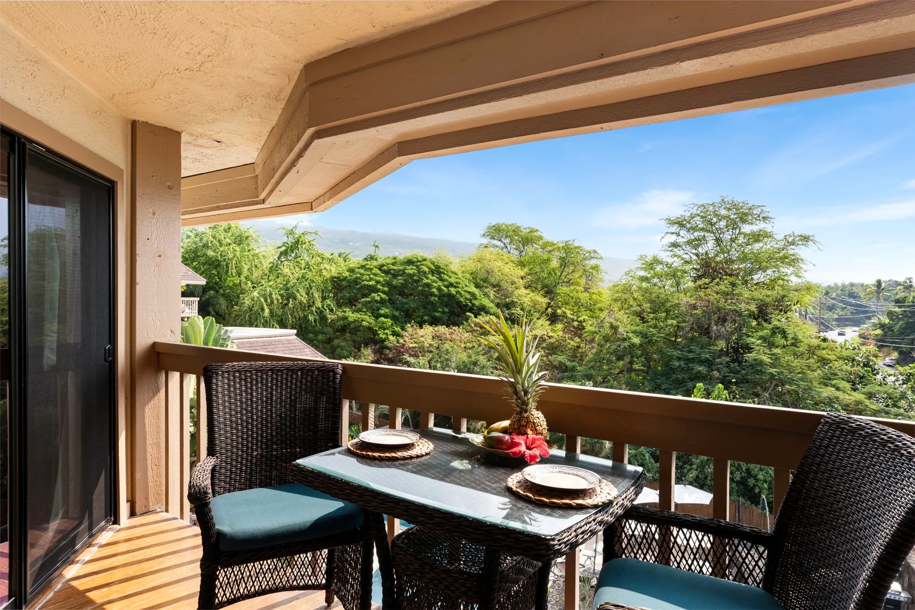A covered balcony has a dining table and seating overlooking green trees.