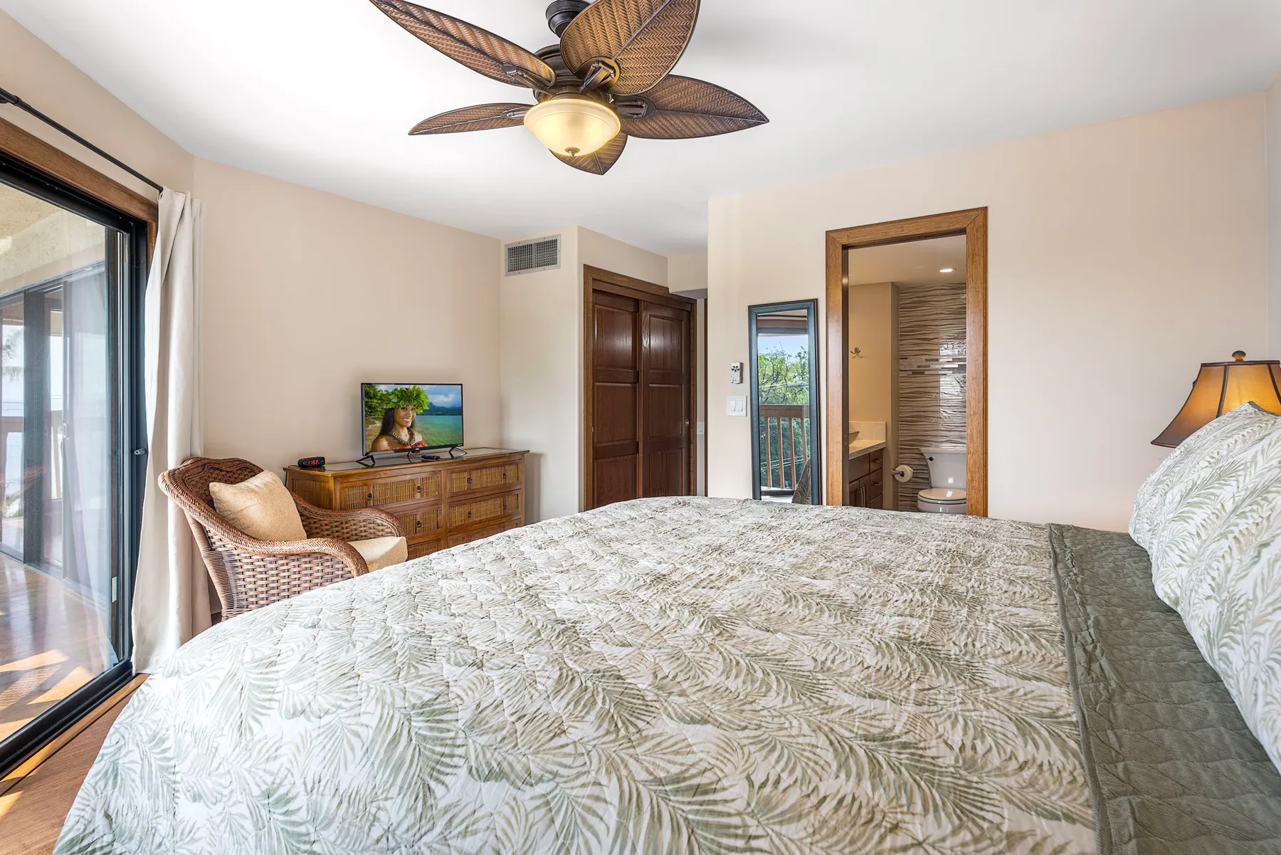 A bedroom with a bed, woven seating, and a ceiling fan.