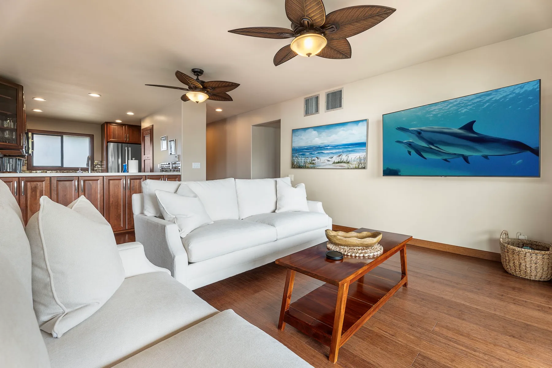 A living room with white seating and framed ocean artwork.