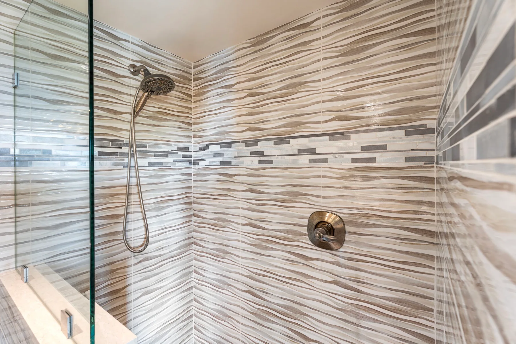 A tiled shower with a mounted showerhead and wall controls.