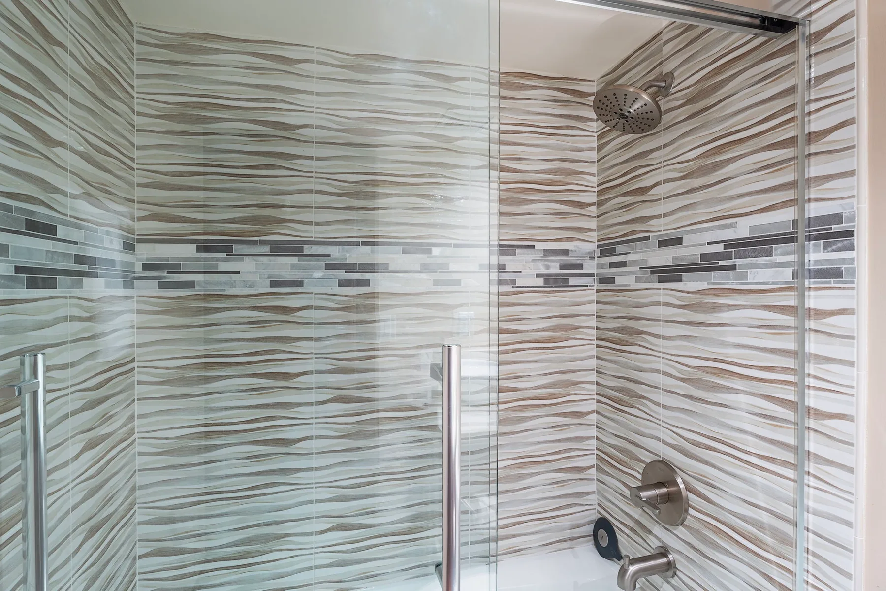 A tiled shower with a glass panel and a handheld shower fixture.