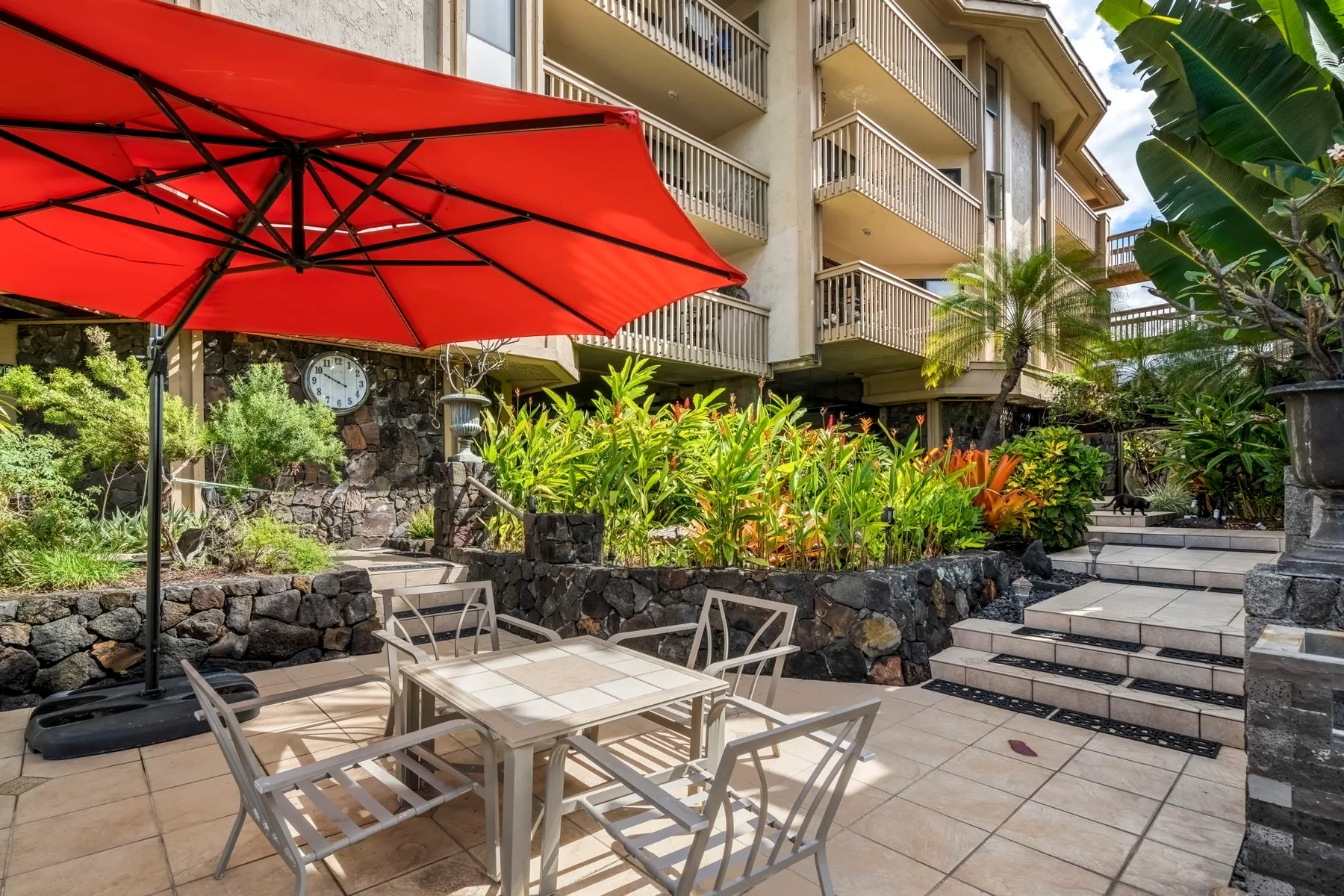 An outdoor patio with dining seating beneath a large red umbrella.