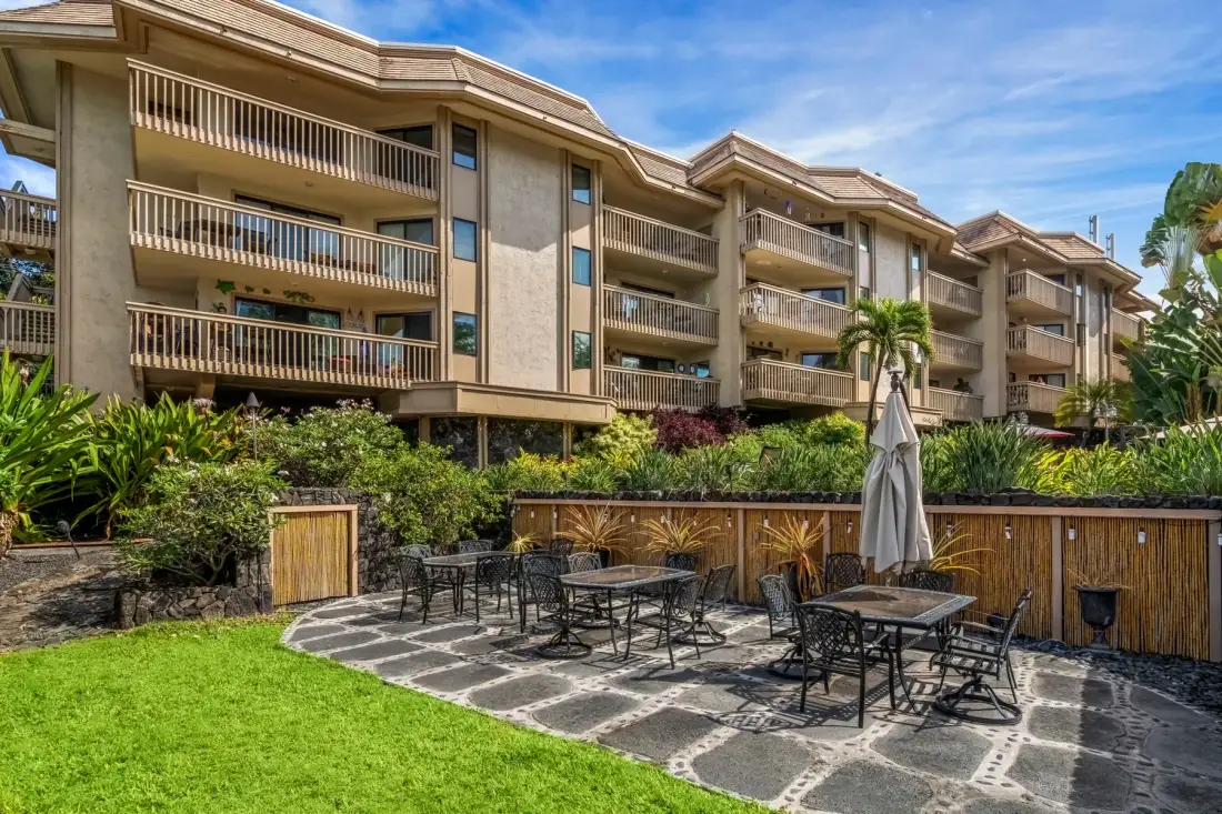 Outdoor patio with tables and seating beside a landscaped lawn.