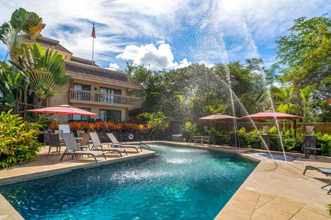 An outdoor swimming pool with lounge seating and red umbrellas beside a building.