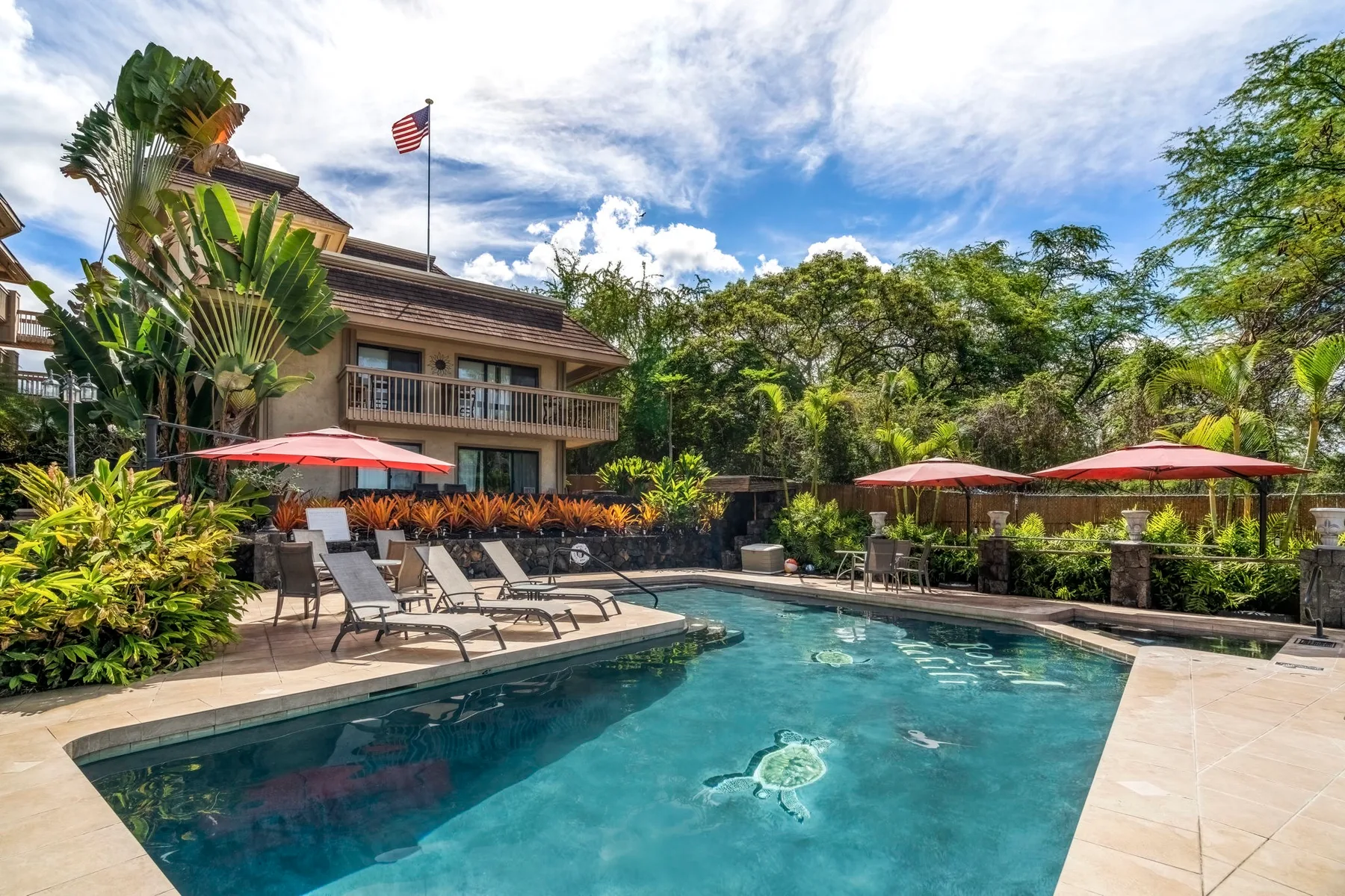 An outdoor swimming pool beside a landscaped patio with lounge seating and umbrellas.