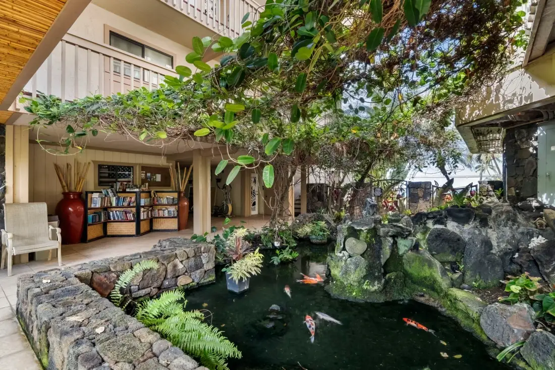A landscaped courtyard pond with koi sits beside a building and outdoor seating.