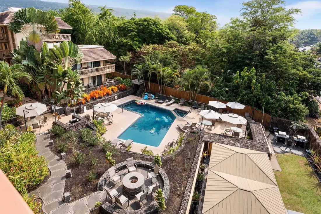 An outdoor pool area is surrounded by seating, greenery, and resort-style buildings.