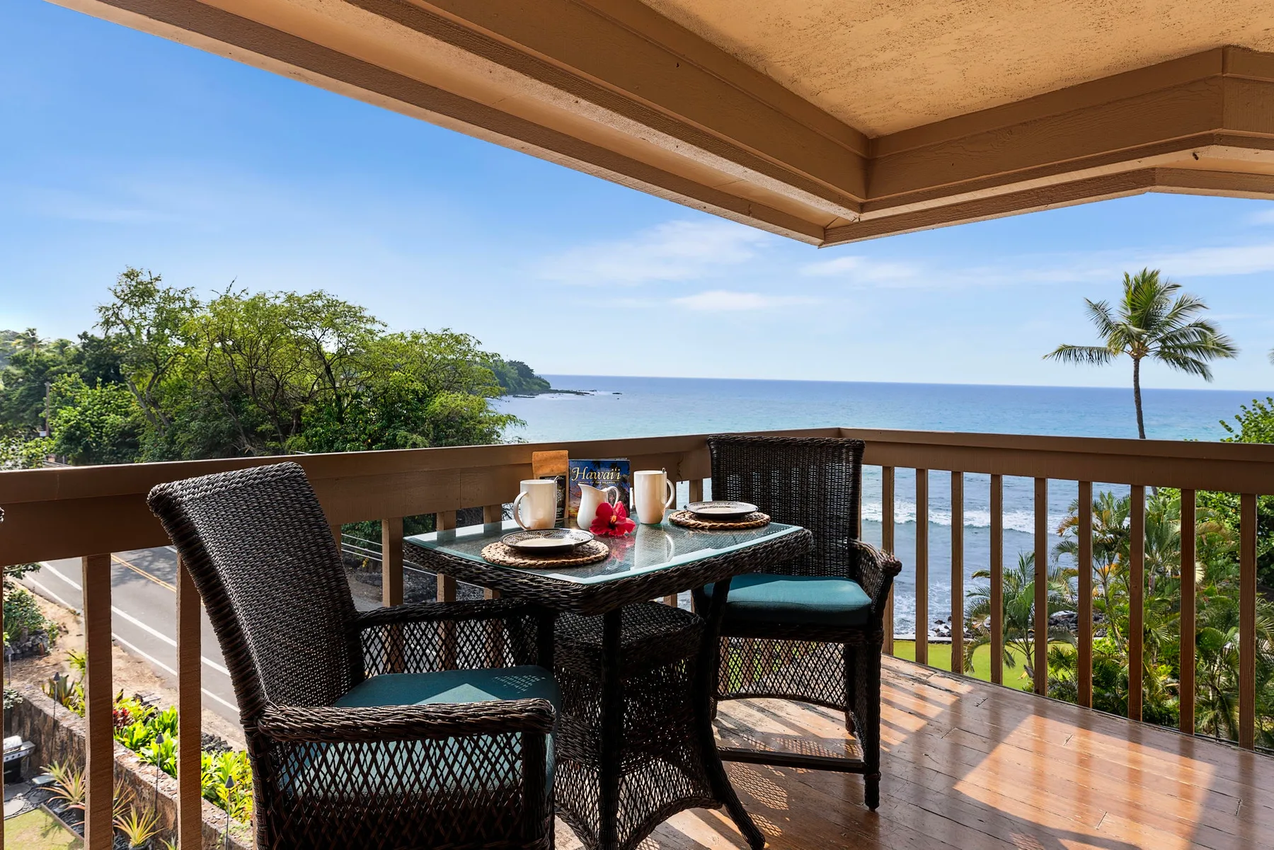 A covered balcony has a dining table and seating overlooking the ocean.