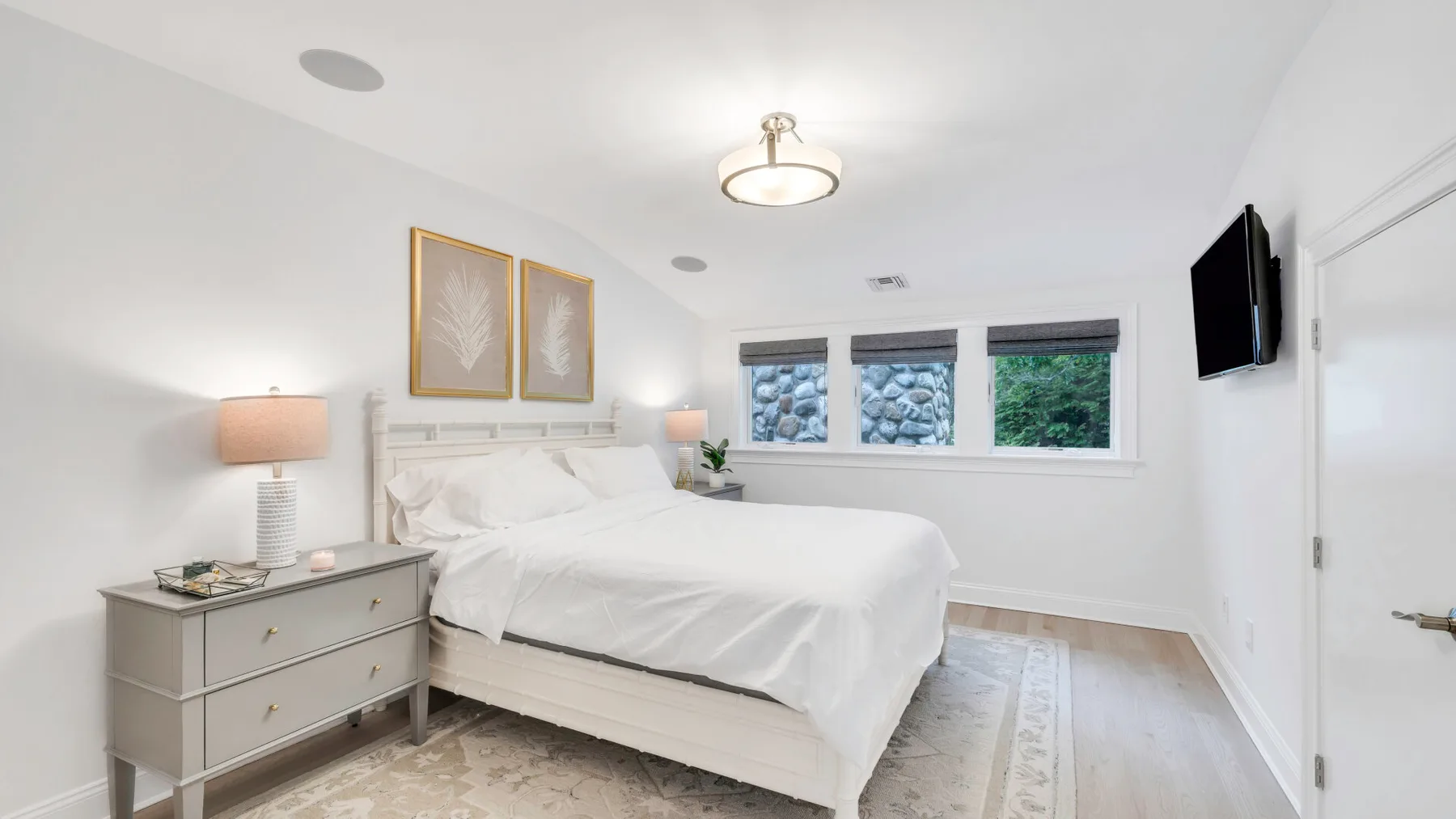 A bright bedroom with a neatly made bed and windows overlooking greenery.