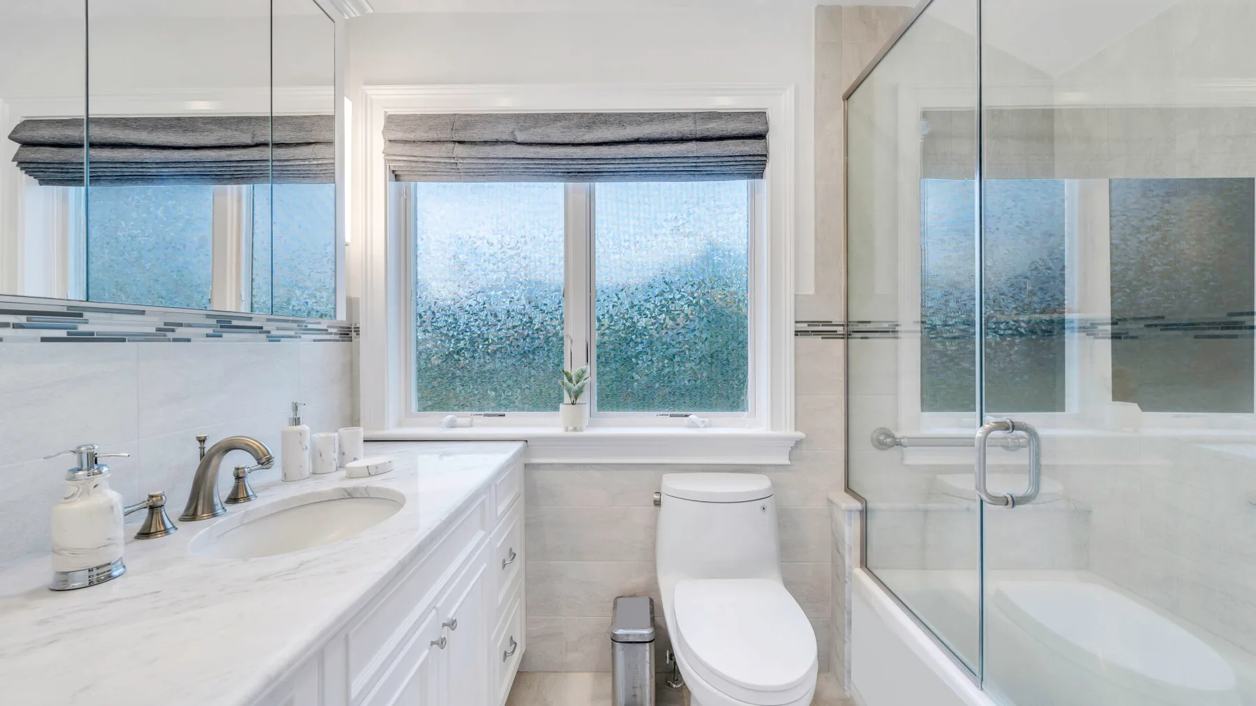 A bright bathroom with a long vanity, a toilet, and a glass-enclosed shower.