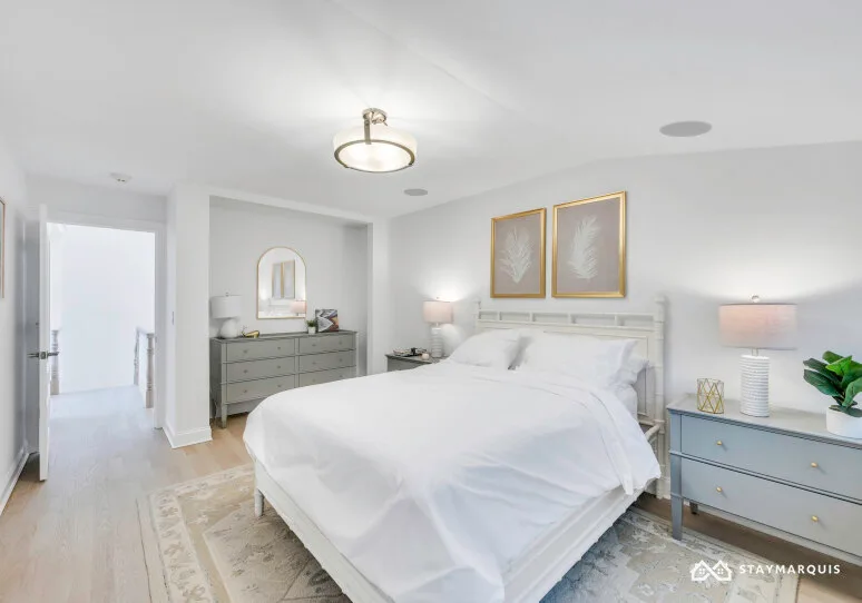A bright bedroom with a white bed and matching bedside tables.