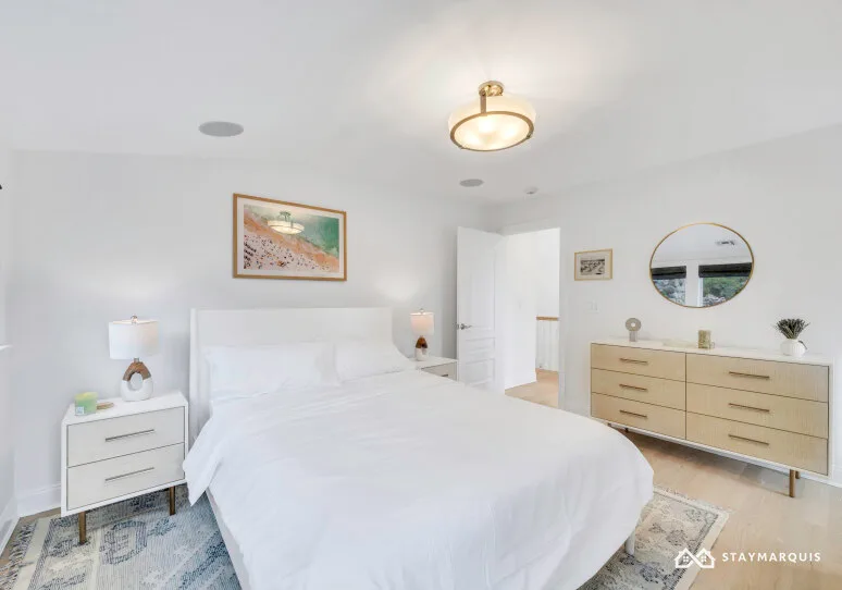 A bright bedroom with a large bed, bedside tables, and a dresser.