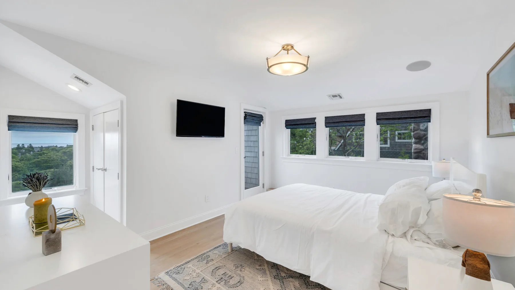A bright bedroom with white bedding and windows along the wall.