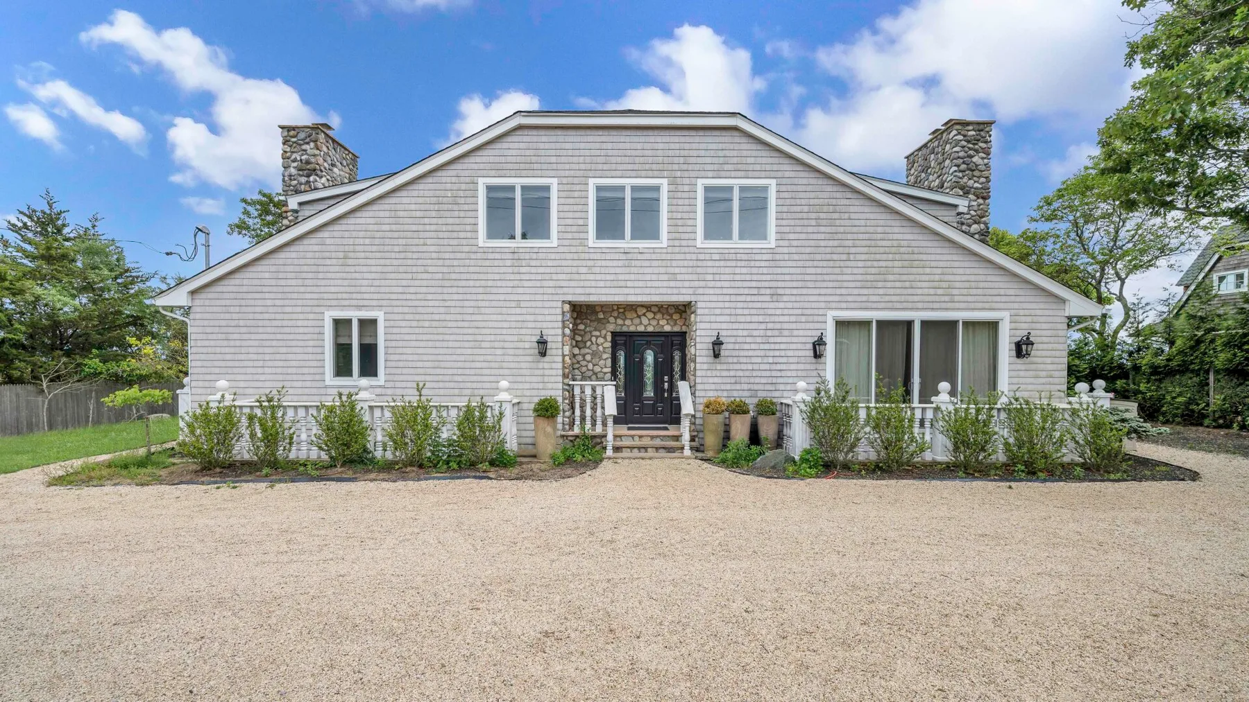 A large light-colored house with several windows faces a broad gravel driveway.