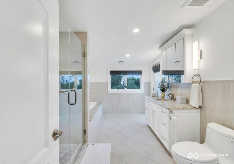 A bright bathroom with a glass shower, vanity, and window.