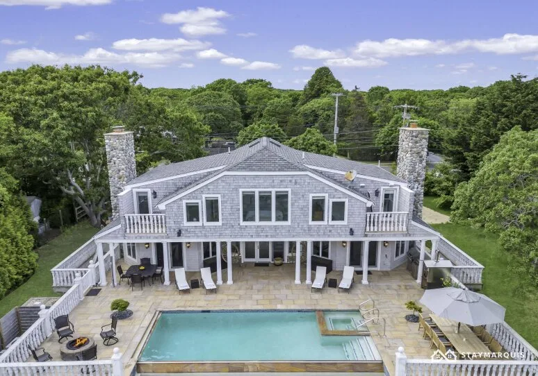A large house overlooks a backyard pool and paved patio.