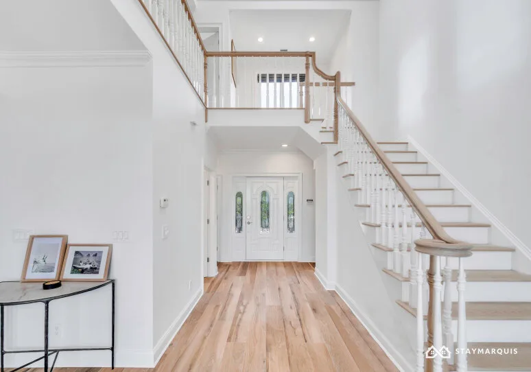 A bright entry hall with a wooden staircase and white double doors.