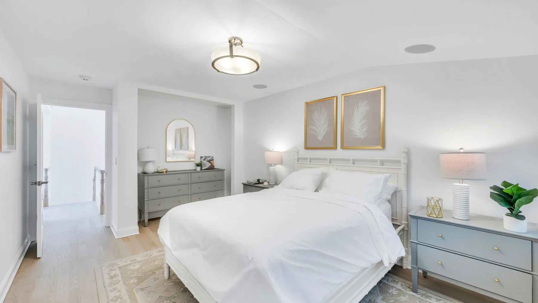 A bright bedroom with a neatly made bed, bedside tables, and framed wall art.