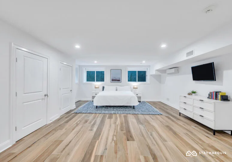 A bright bedroom with a bed centered beneath three windows.