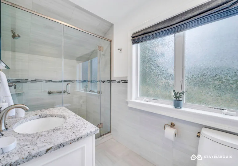 A bright bathroom with a glass shower, vanity, and frosted window.