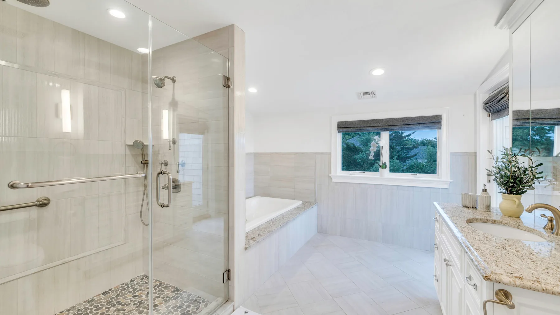 A bright bathroom with a glass shower, soaking tub, and vanity.