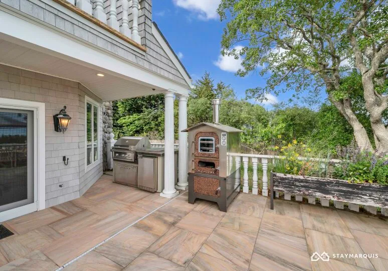 A tiled outdoor patio with a grill and a freestanding oven beside the house.