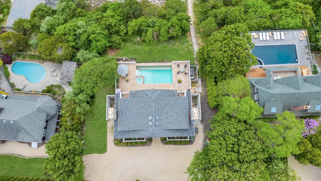 Aerial view of several buildings surrounded by trees, with swimming pools nearby.