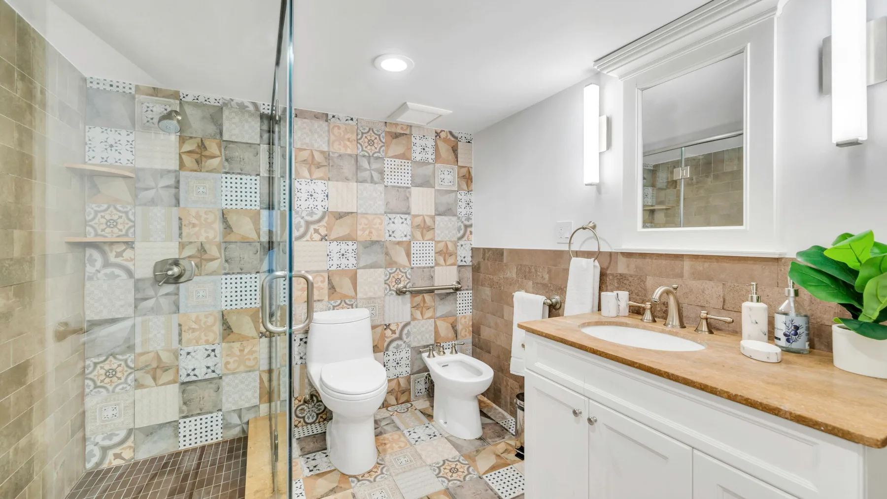 A tiled bathroom with a glass shower, toilet, bidet, and vanity.