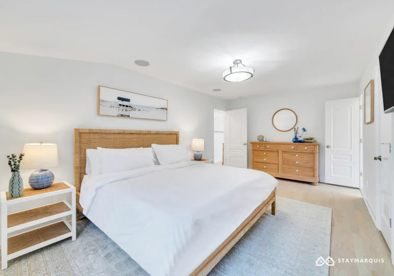 A bright bedroom with a white bed, wooden headboard, and matching dresser.