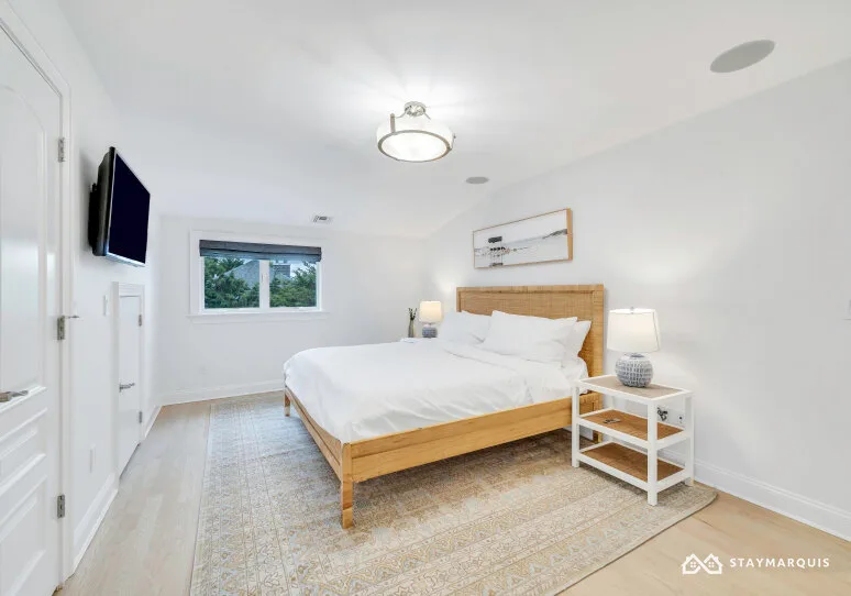 A bright bedroom with a wooden bed, white bedding, and a bedside table.