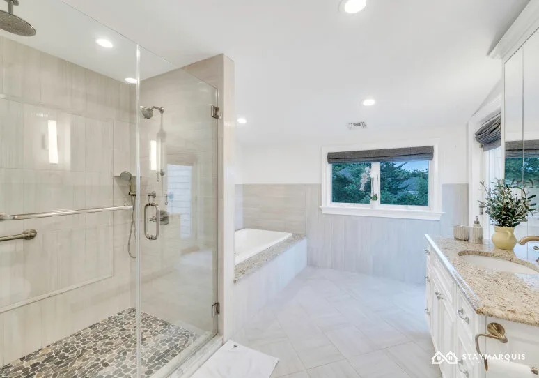 A bright bathroom with a glass shower, bathtub, and window.