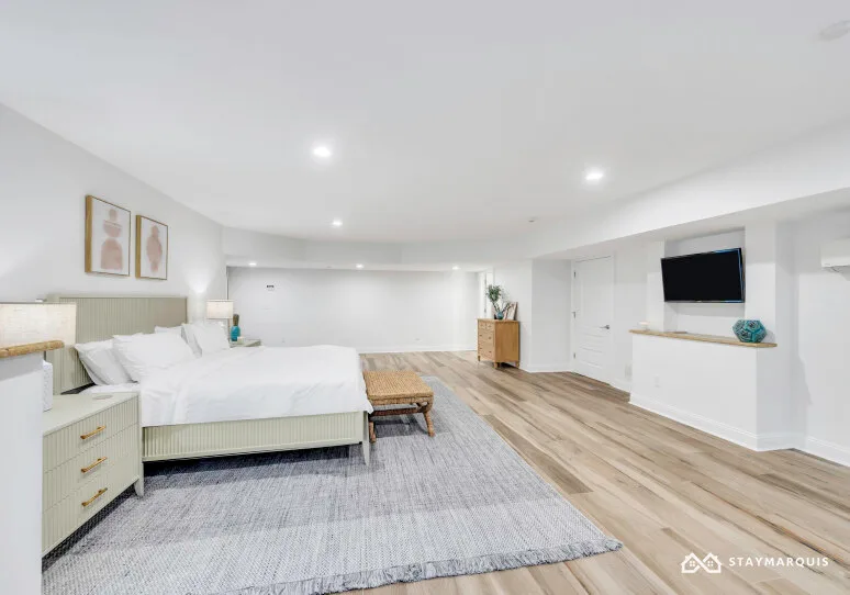 A bright bedroom with a bed, rug, and wall-mounted television.