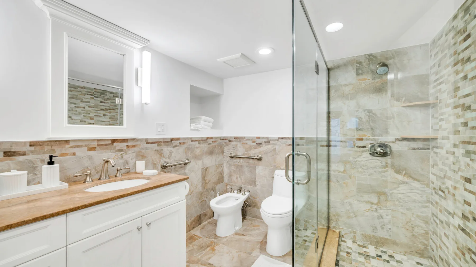 A bright bathroom with a wood-toned vanity and a glass-enclosed shower.