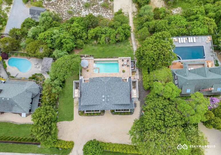 An aerial view shows a house with a swimming pool surrounded by greenery.