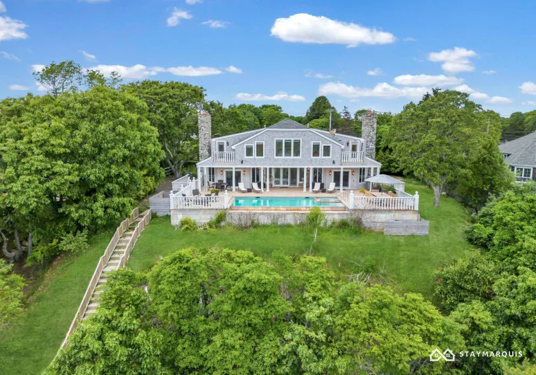 A large house with a pool and deck stands amid green trees.