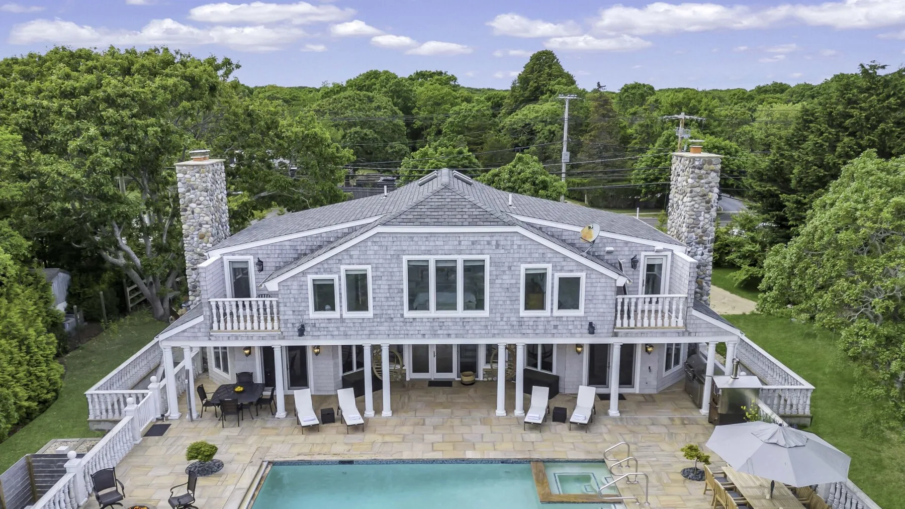 A large house faces a stone patio with an outdoor swimming pool.