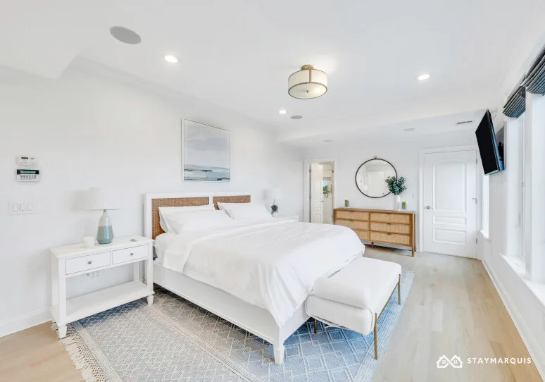 A bright bedroom with a neatly made bed and light-colored furnishings.